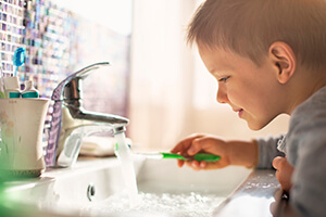 Young boy holding toothbrush under running water