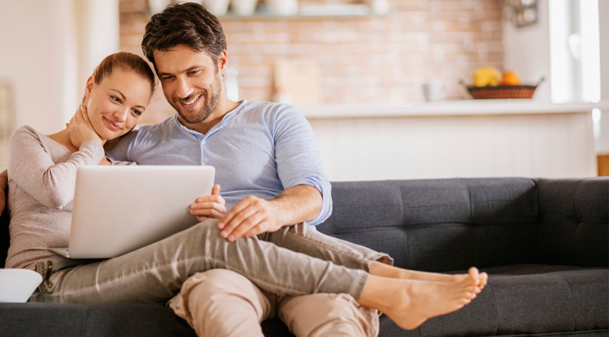 Man and woman sitting on couch together and looking at laptop