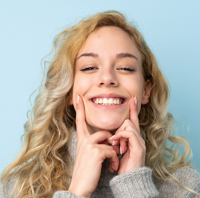 Young blonde woman pointing to her flawless smile after cosmetic dentistry in Sparks