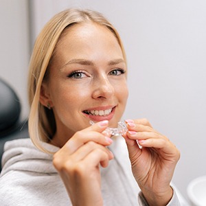 Closeup of woman smiling while holding clear aligner