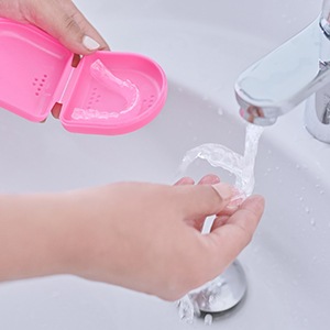 Patient rinsing clear aligner in sink