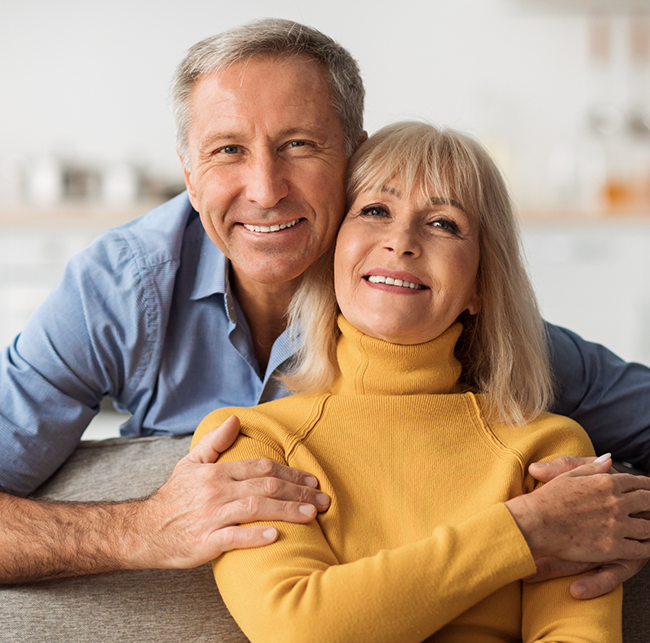 Older couple smiling at home after replacing missing teeth in Sparks