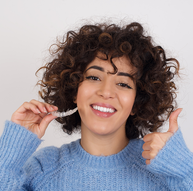 Smiling woman giving a thumbs up while holding clear aligners in Sparks