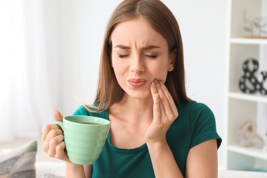 A woman experiencing tooth sensitivity while drinking coffee